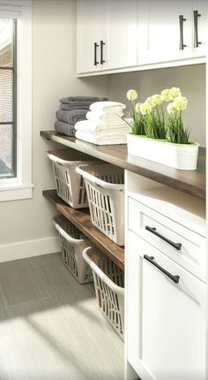 an organized laundry room with white cabinets and baskets on the shelves, along with flowers