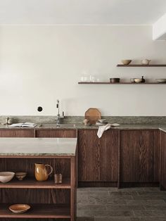 a kitchen with wooden cabinets and marble counter tops, along with shelves on the wall