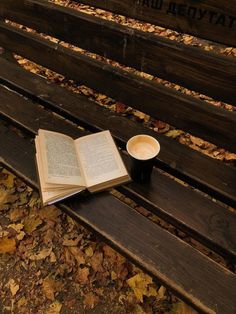 an open book sitting on top of a wooden bench next to a cup of coffee