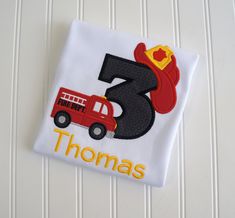 a birthday shirt with a firetruck and hat on it's front, the number three is for thomas