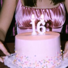 a woman holding a cake with candles in the shape of 16 on top of it