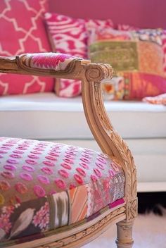 an ornate wooden chair with colorful pillows on it's back and sides, in front of a white couch