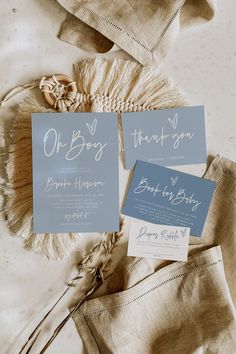 wedding stationery with blue and white cards on top of the cloths, next to an old - fashioned hat