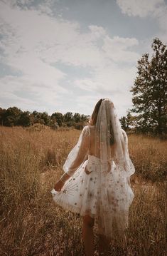 a woman in a white dress is walking through the grass with her veil over her head