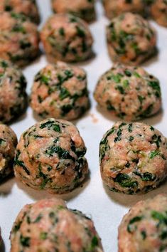 several balls of meat with spinach and cheese on top are sitting on a baking sheet