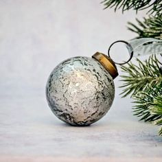 a glass ornament hanging from a christmas tree with snow on it's surface