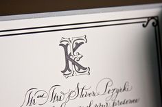 the letter k is inscribed in cursive writing on a white card with black ink