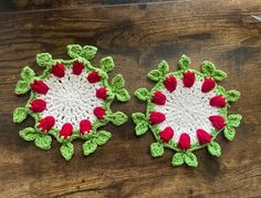 two crocheted coasters with red and green flowers on them sitting on a wooden table