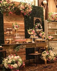 a table topped with lots of cake and flowers next to a wall covered in greenery