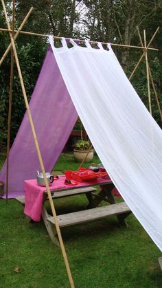 a purple and white tent sitting on top of a lush green field next to a picnic table