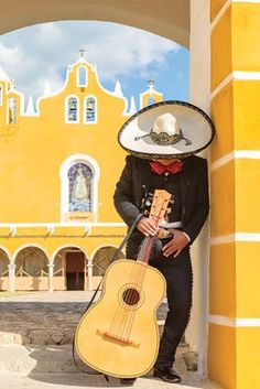 a man wearing a sombrero and holding an acoustic guitar in front of a yellow building