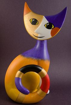 a colorful cat figurine sitting on top of a purple surface with an orange and yellow ring around it's neck