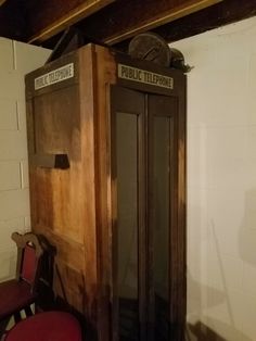 an old fashioned public telephone booth in the corner of a room with two red chairs