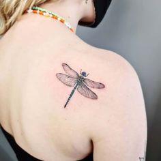 a woman's back shoulder with a dragonfly tattoo on the upper part of her body