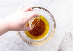 someone is adding olive oil to the mixture in a glass bowl with whisk