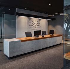 the front desk of an office with three laptops on it and glass walls behind it