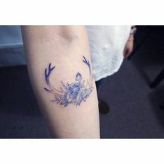 a woman's arm with an arrow and flowers tattoo on it, in blue ink