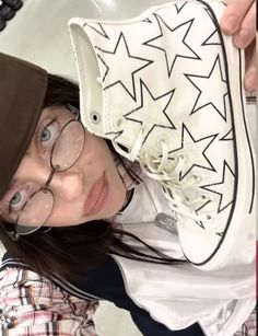 a woman wearing glasses and a hat holding up a pair of shoes