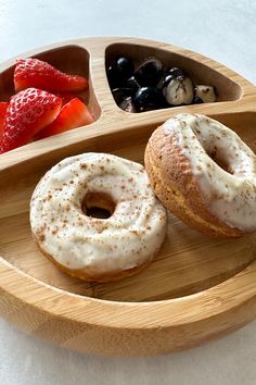 two donuts are on a wooden plate with strawberries and berries in the background