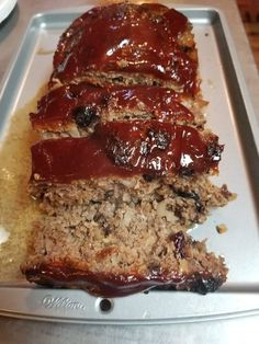 sliced meatloaf sitting on top of a pan covered in ketchup and sauce