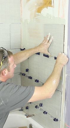 a man in grey shirt and yellow headband fixing tile on the walls of a bathroom