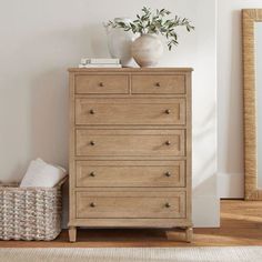 a white vase sitting on top of a wooden dresser next to a basket and mirror