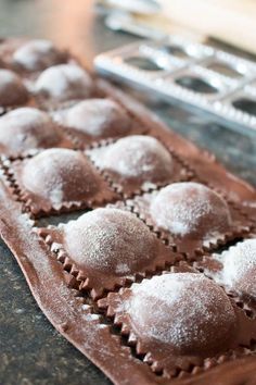 chocolate pastries sitting on top of a cookie sheet with powdered sugar in the middle