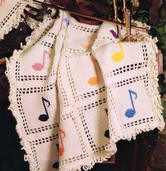 a crocheted blanket with musical notes on it hanging from a hook in front of a wall