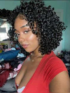 a close up of a person with curly hair in a room and clothes on the floor