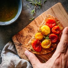 a person holding a piece of bread with tomatoes on it