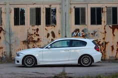 a white car is parked in front of an old building with rusted paint on it