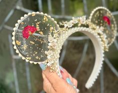 a person holding up a pair of headbands with flowers on the side and pearls around them