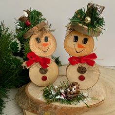 two wooden snowmen sitting on top of a piece of wood next to pine cones