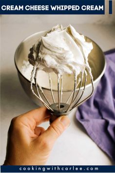 a hand holding a wire whisk over a bowl with whipped cream in it