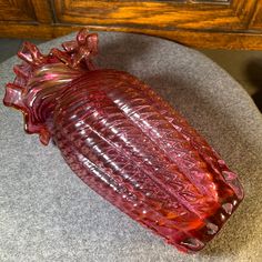 a red glass vase sitting on top of a gray ottoman next to a wooden dresser