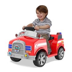 a young boy riding on the back of a red toy firetruck with wheels