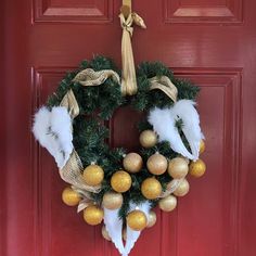 a christmas wreath hanging on a red door with gold balls and feathers around the wreath