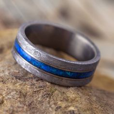 a wedding band with blue opal inlays sits on top of a rock