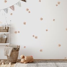 a teddy bear sitting on the floor in front of a wall with flowers and bunting