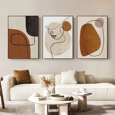 three abstract paintings hang on the wall above a white couch and coffee table in a modern living room