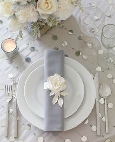 the table is set with white plates and silverware, napkins and flowers on them