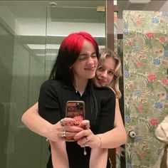 two women taking a selfie in front of a mirror with their cell phones together