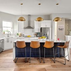 a large kitchen with white cabinets and gold pendant lights hanging from the ceiling, along with bar stools