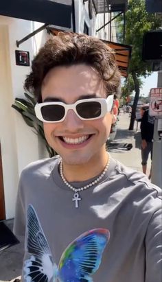 a man with sunglasses on taking a selfie in front of a building and smiling at the camera