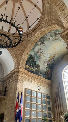 an ornate ceiling with paintings and chandelier in a church setting, including two flags hanging from the ceiling