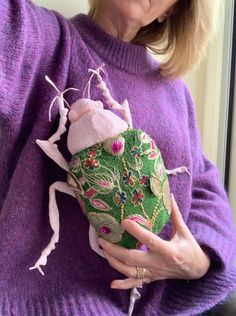 an older woman is holding a green and pink object in her right hand while wearing a purple sweater