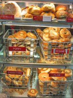 several baskets of doughnuts on display in a bakery case with labels reading poppy, poppy and sesame