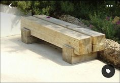 a wooden bench sitting on top of a cement ground next to trees and bushes with purple flowers in the background