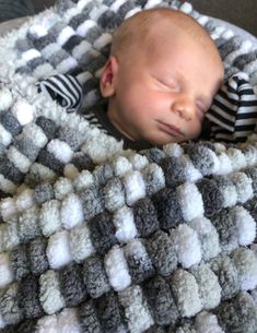 a baby sleeping on top of a blanket covered in white and gray crochet