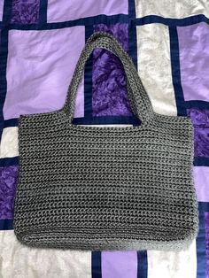 a gray crocheted purse sitting on top of a purple and white quilted bed